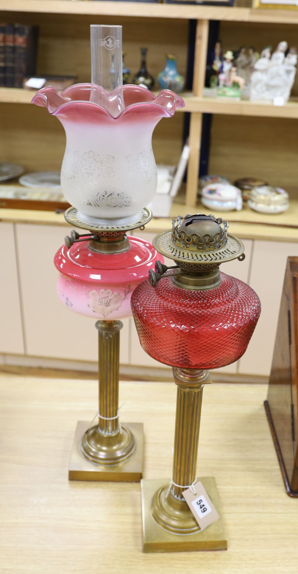 A brass column oil lamp with cranberry glass reservoir and frilled frosted and pink glass shade and a similar oil lamp